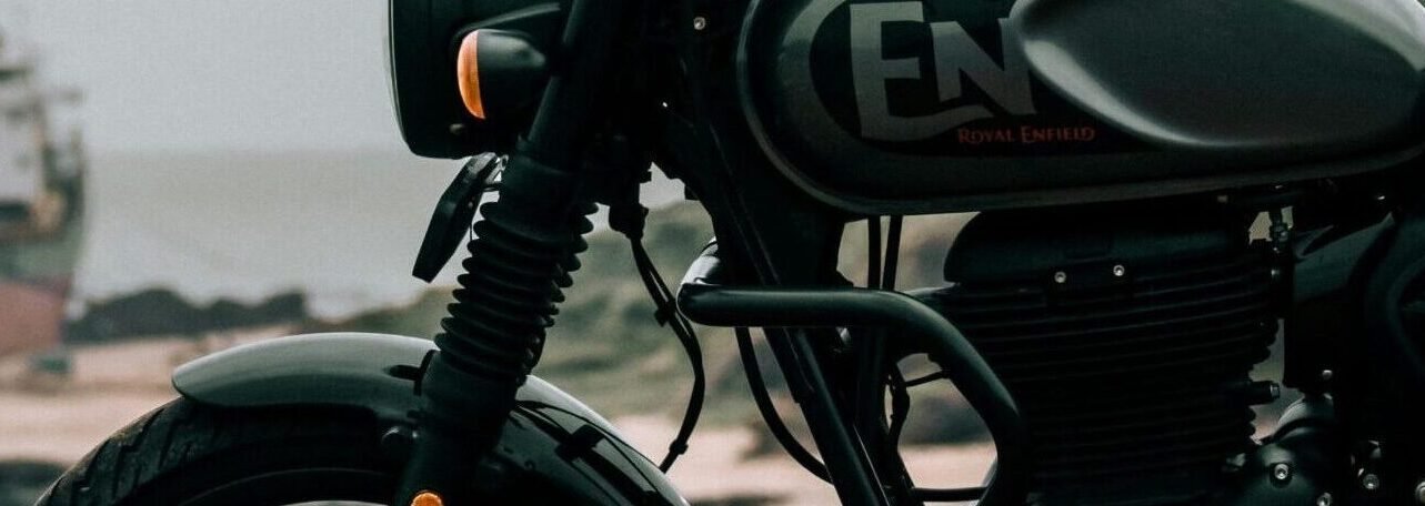 Vertical shot of a Royal Enfield motorcycle on a coast, with a ship in the background.